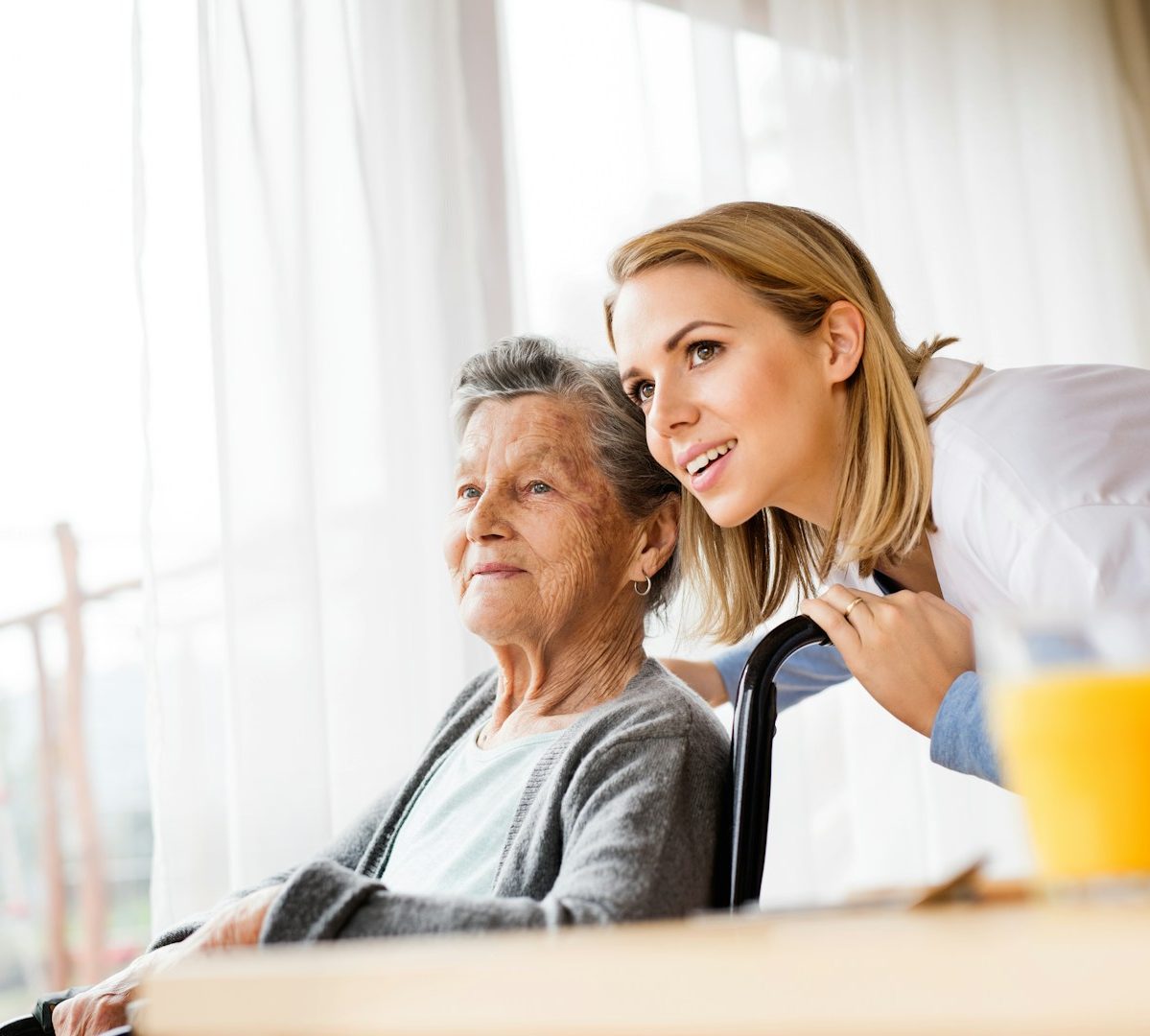 Frau im Rolstuhl mit Pflegerin Ältere Dame im Rollstuhl. eine Pflegerin beugt sich auf Augenhöhe.